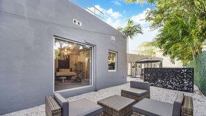 A modern outdoor seating area with wicker furniture and a glass wall overlooking a bedroom. - Designer Studio | Close to Wynwood | Design District  | Downtown (Miami)