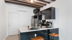 A modern kitchen with a white countertop, dark backsplash, and two wooden bar stools. - Designer Studio | Close to Wynwood | Design District  | Downtown (Miami)