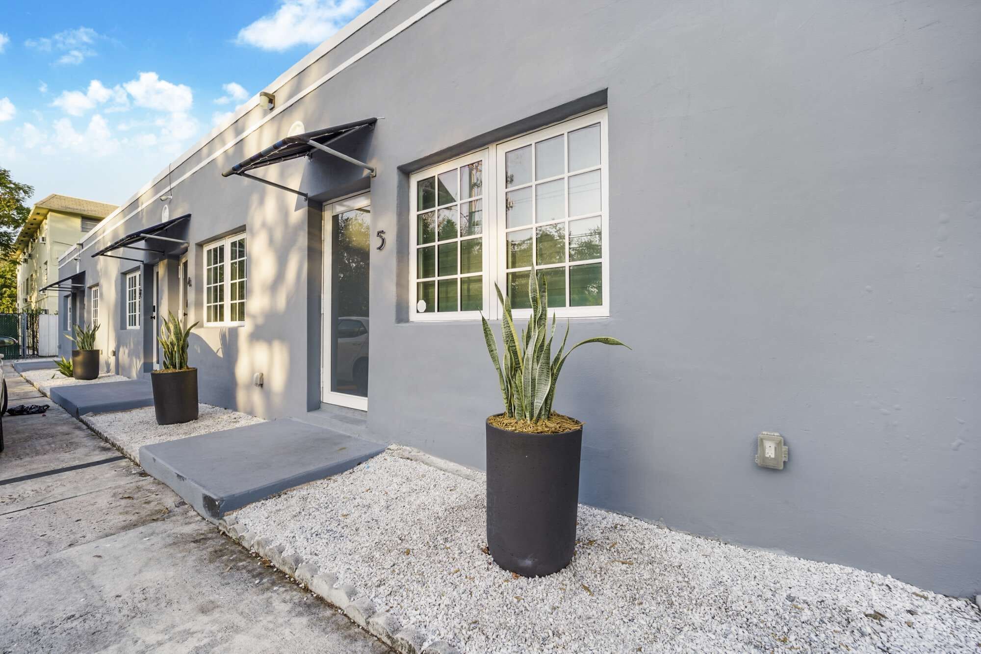 Un edificio moderno con grandes ventanales, fachada gris y plantas en macetas al frente.