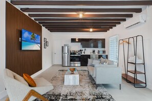 A modern living room with a flat-screen TV, a sofa, a coffee table, and a kitchen area with appliances. - Designer Studio | Close to Wynwood | Design District  | Downtown (Miami)