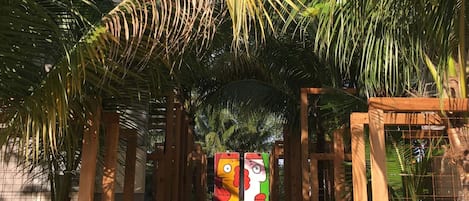 En sti der fører til en port med et farverigt mural, omgivet af frodig vegetation og en klar blå himmel.