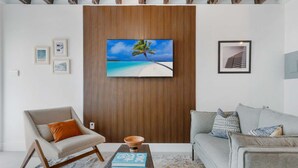 Un soggiorno moderno con una grande TV montata su un pannello parete in legno, due divani con cuscini, un tavolino da caffè con un libro e quadri appesi alle pareti.