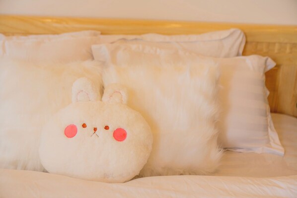 A bed with white bedding and a plush toy resembling a white animal with pink eyes and ears.