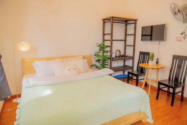 A hotel room with a bed, a desk, two chairs, a small table, a potted plant, a TV, and a fan. - Yori House (Lam Vien - Da Lat)