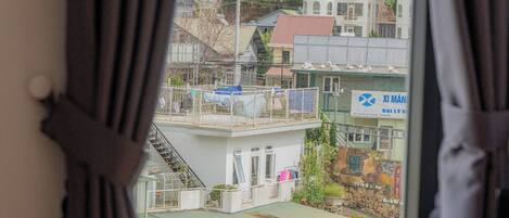 Habitación con ventana que da a una zona residencial, una mesita redonda con una planta y cortinas corridas a un lado.