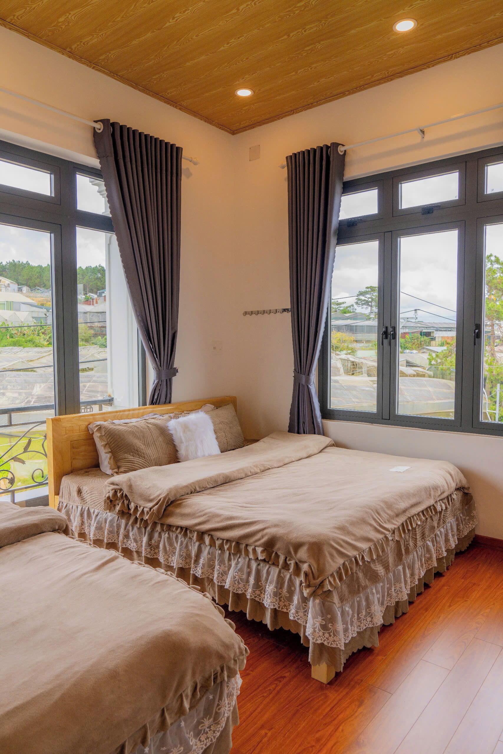 Quarto com duas camas, cabeceiras de madeira e janelas amplas com cortinas.