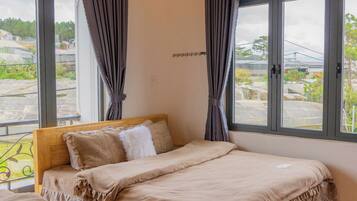 Quarto com duas camas, cabeceiras de madeira e janelas amplas com cortinas.