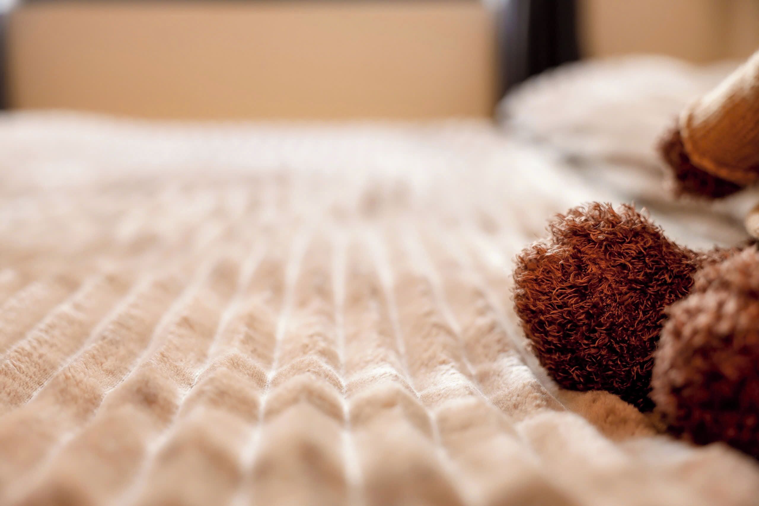 A close-up of a textured beige fabric, possibly a bedspread or blanket, with a ribbed pattern.