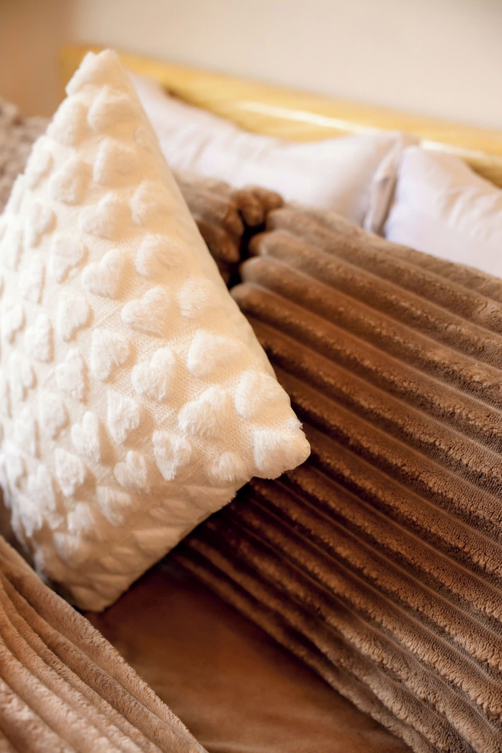 A bed with a textured white pillow and a brown striped blanket.