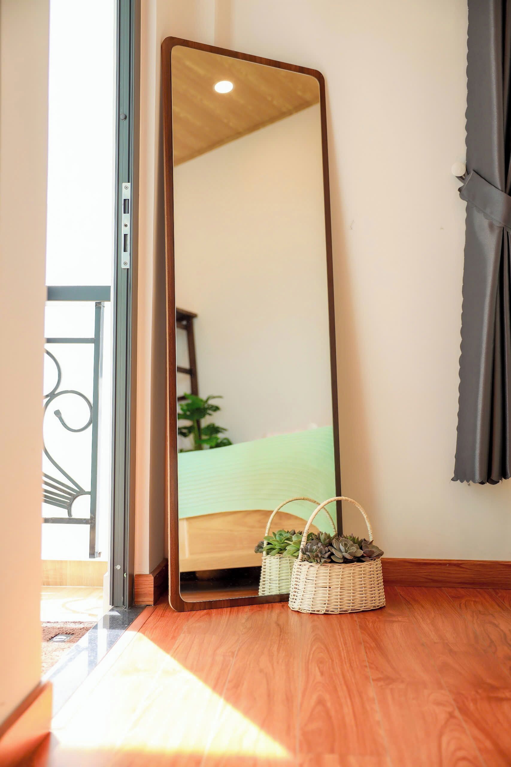 Une pièce dotée d’un grand miroir, d’un plancher en bois, d’un lit recouvert d’une couverture verte et de deux paniers en osier contenant des plantes.