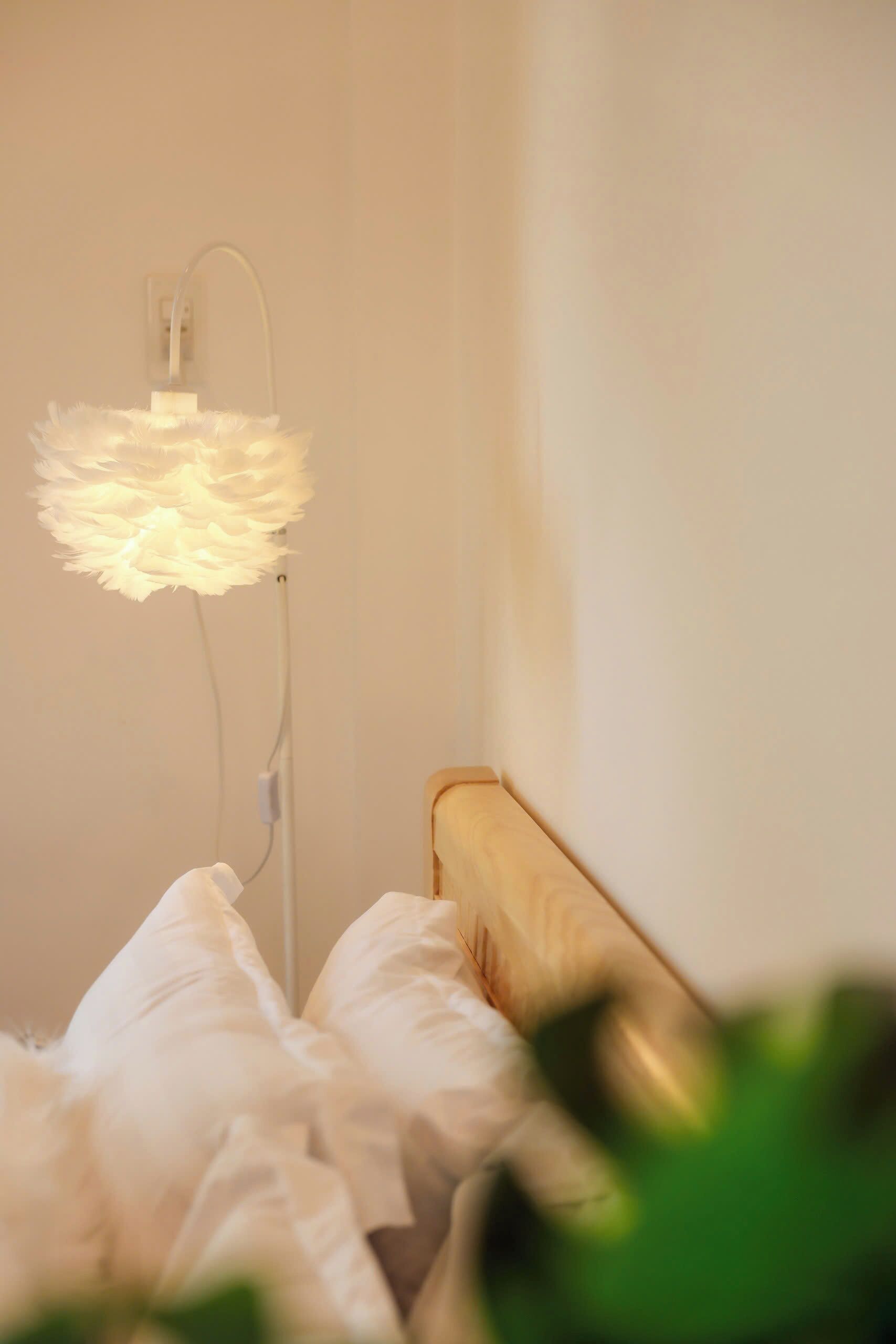 A bed with white bedding and a white, fluffy, illuminated lamp on a bedside table.