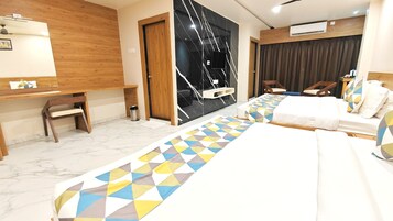 A hotel room with a long bed, a desk, and a chair. There is a wall-mounted TV and an air conditioning unit.