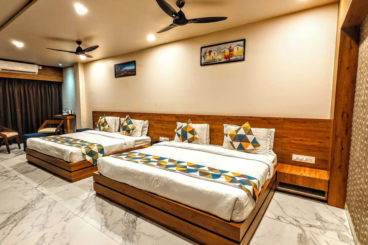 A hotel room with two beds, a ceiling fan, an air conditioning unit, a wooden headboard, a marble floor, and a small table with chairs.