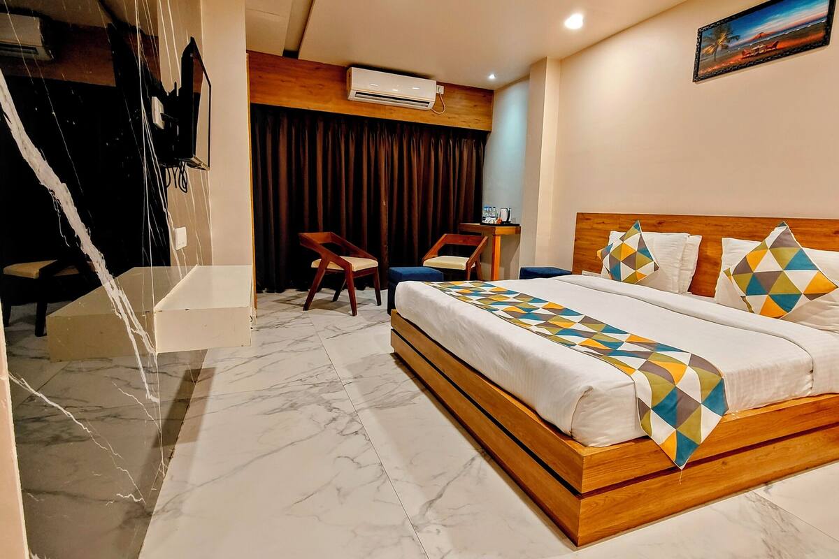 A hotel room with a wooden bed, a marble floor, a desk with a chair, and a window with curtains.