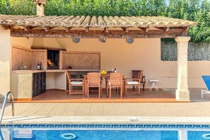 Eine Außenküche mit Sitzgelegenheit am Pool, einem integrierten Grill und Blick auf den Pool.