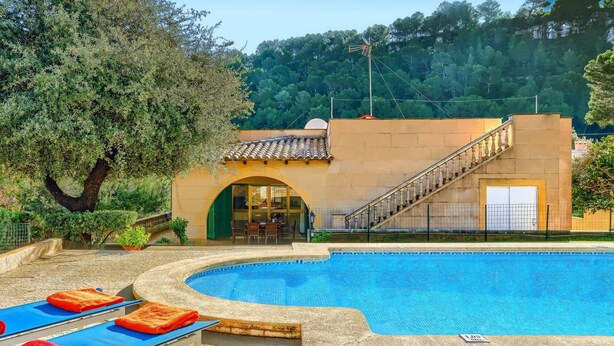 Ein Poolbereich mit einem Steinebecken, Liegestühlen und einer Treppe, die zu einem Gebäude mit Bogenöffnung führt.