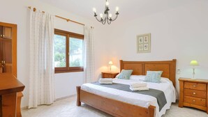 Ein Schlafzimmer mit einem hölzernen Bett, zwei Nachttischen, einem Beistelltisch, einer Pendelleuchte, einem Fenster mit Vorhängen und einer Wanddekoration.