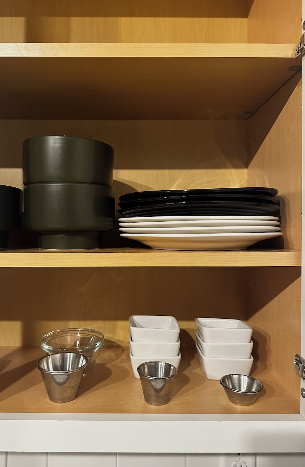 A kitchen shelf with stacked plates, bowls, and a metal container.