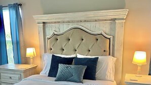 A bedroom with a tufted headboard, a large bed with white bedding, two bedside tables with lamps, and a window with blue curtains. - Charming Suite in a Spacious Shared Home in Fishers – Utilities included (Fishers)