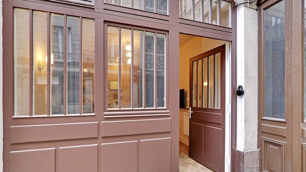 A brown-framed door with a glass panel, a visible interior hallway, and a light fixture. - Cozy studio - 2P - Gare de l'Est (Paris)