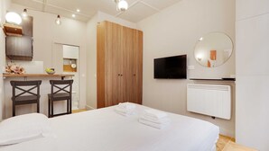 A bedroom with a bed, two chairs, a wooden wardrobe, a TV, and a mirror. - Cozy studio - 2P - Gare de l'Est (Paris)