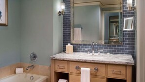 A bathroom with a bathtub, a sink with a mirror, and a vanity with drawers and a towel rack.