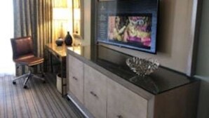 A hotel room with a flat-screen TV mounted on a cabinet, a chair, and a lamp on a table.