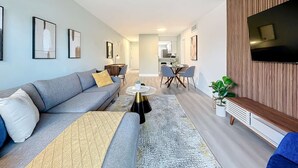 Una sala de estar moderna con un sofá gris, una mesita de centro y un televisor montado en una pared de paneles de madera.