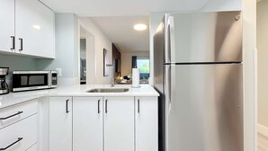 Una cocina moderna con armarios blancos, un refrigerador de acero inoxidable, un microondas y una cafetera.