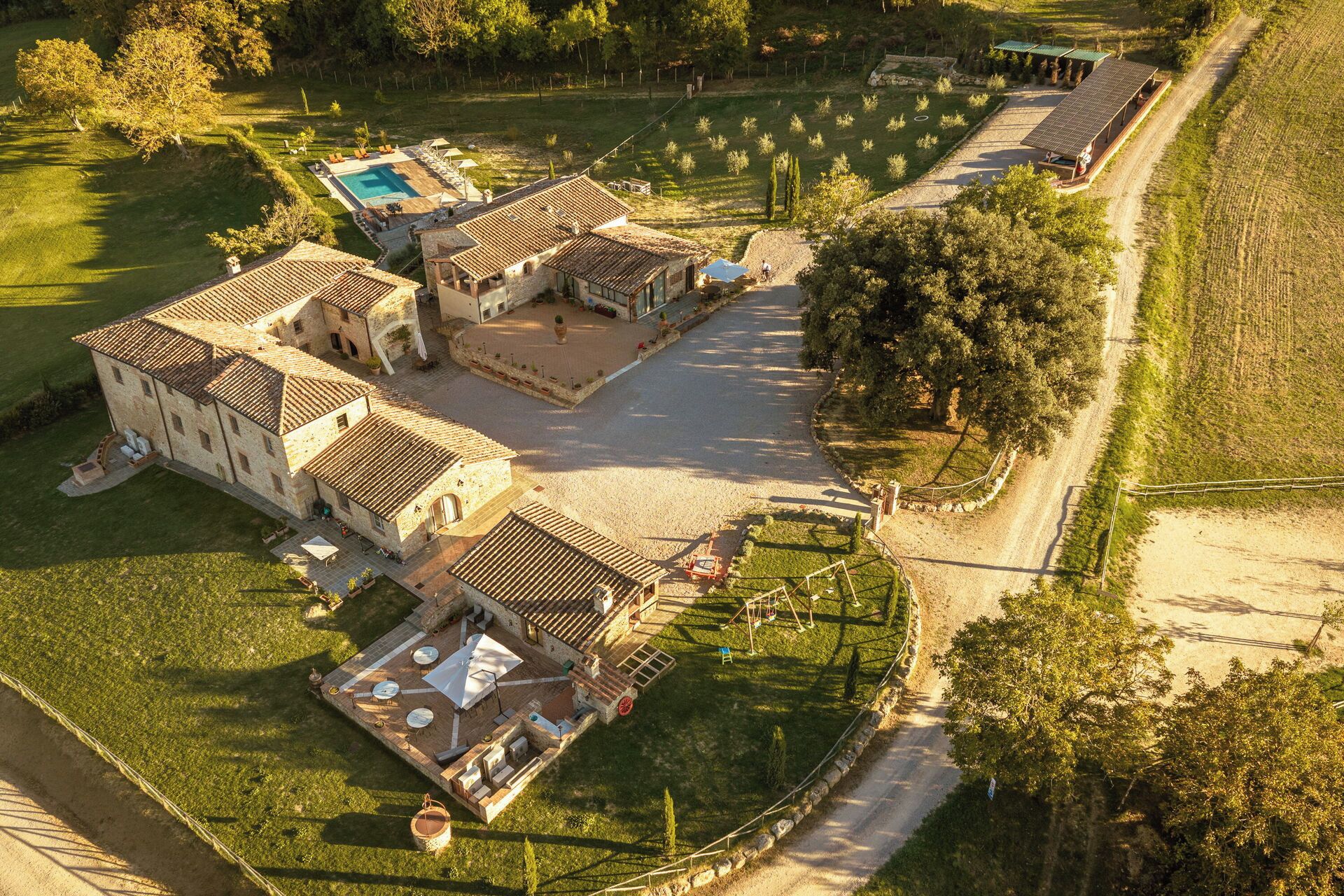 Una vista aerea di una proprietà con piscina, diversi edifici con tetti in terracotta e un giardino curato.