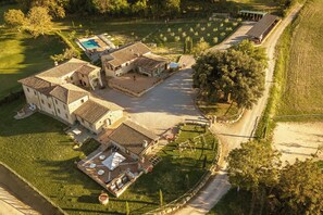 An aerial view of a property with a swimming pool, multiple buildings with terracotta roofs, and a well-maintained garden.
