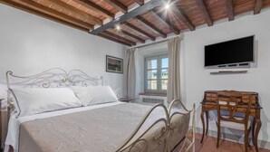 Ein Schlafzimmer mit Bett, Schreibtisch, Stuhl, Fernseher und einem Fenster mit Vorhängen.