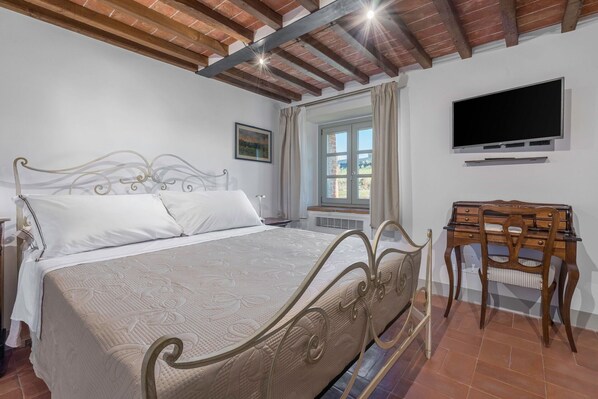 A bedroom with a bed, a desk, a chair, a TV, and a window with curtains.