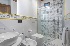 A bathroom with two sinks, a toilet, and a glass-enclosed shower with floral tile patterns.