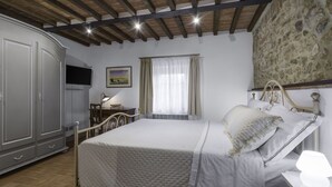 A bedroom with a bed, a desk with a lamp, a wardrobe, and a stone wall. - Il Borgo, Borgo Campassini, Monteriggioni (Monteriggioni)
