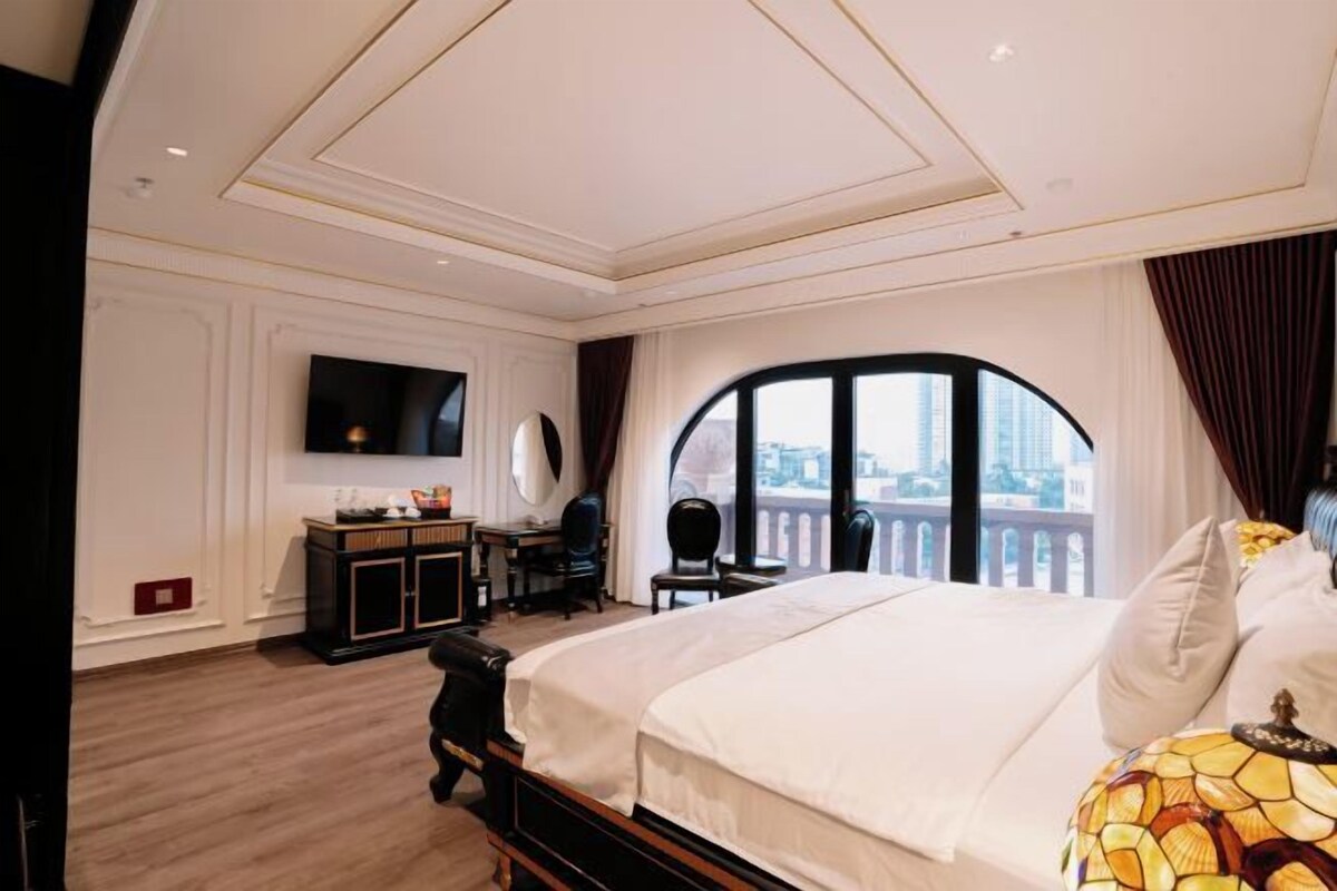 Une chambre d’hôtel avec un grand lit, un bureau avec une chaise, un téléviseur fixé au mur et une vue sur la ville par une grande fenêtre.