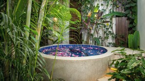 Uma banheira de hidromassagem cercada por vegetação exuberante, um cercado de madeira e uma piscina com azulejos.