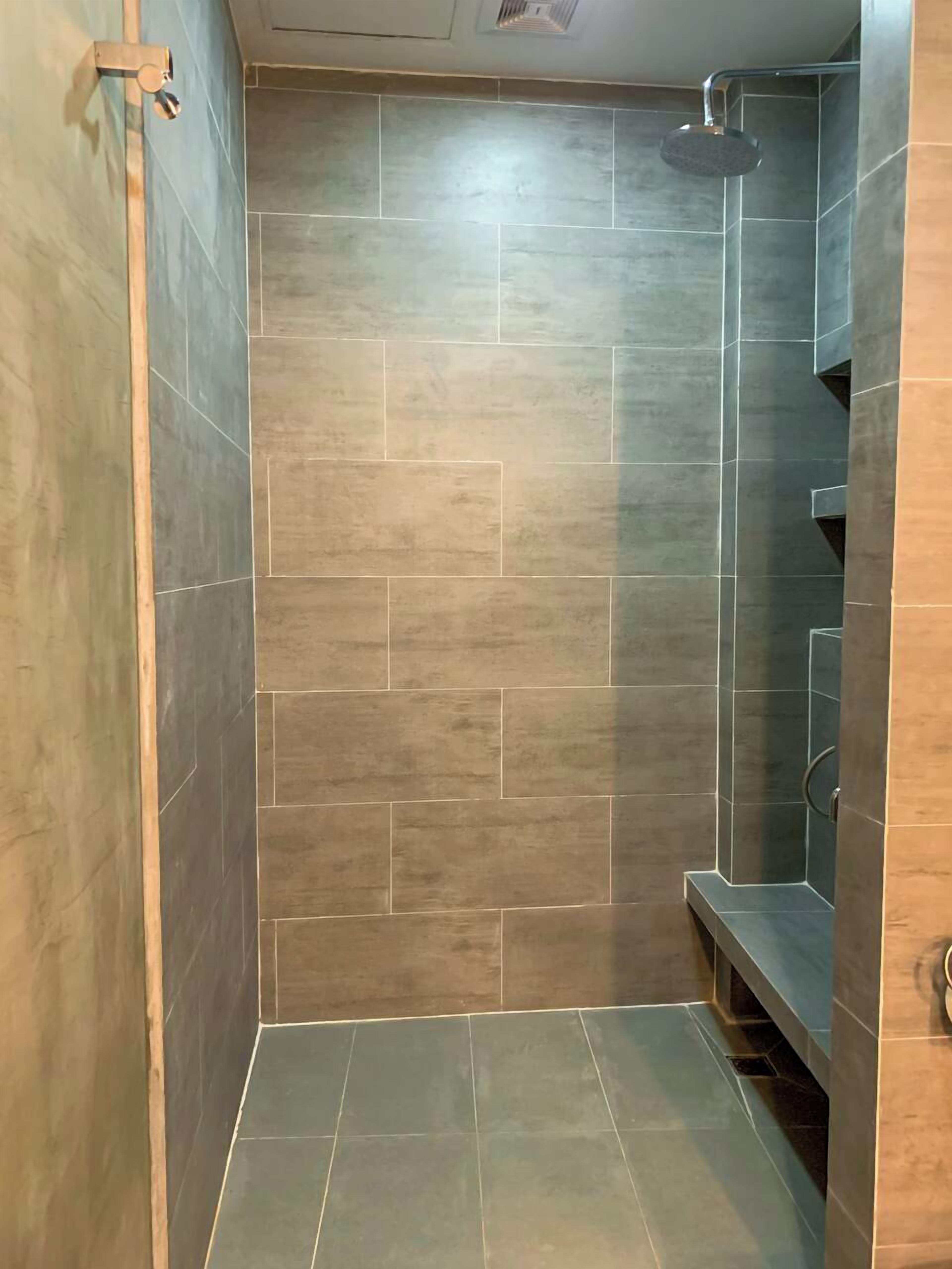 A shower area with a tiled wall and floor, a showerhead, and a metal handrail.