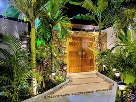 Una puerta de madera con un muro de piedra, rodeada de exuberante follaje tropical.