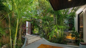 Um jardim interno exuberante com um banco de madeira, um caminho de pedra e uma cerca de bambu.