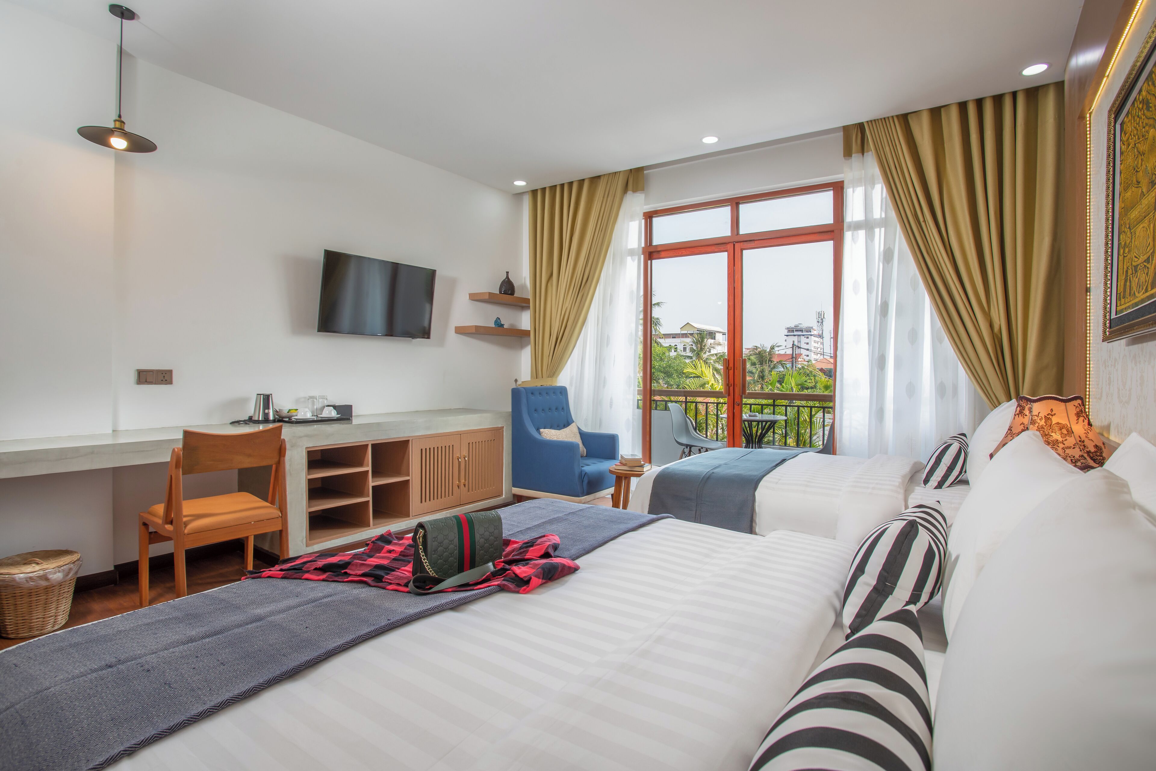Habitación de hotel con cama, escritorio, silla, televisor y balcón con vistas.