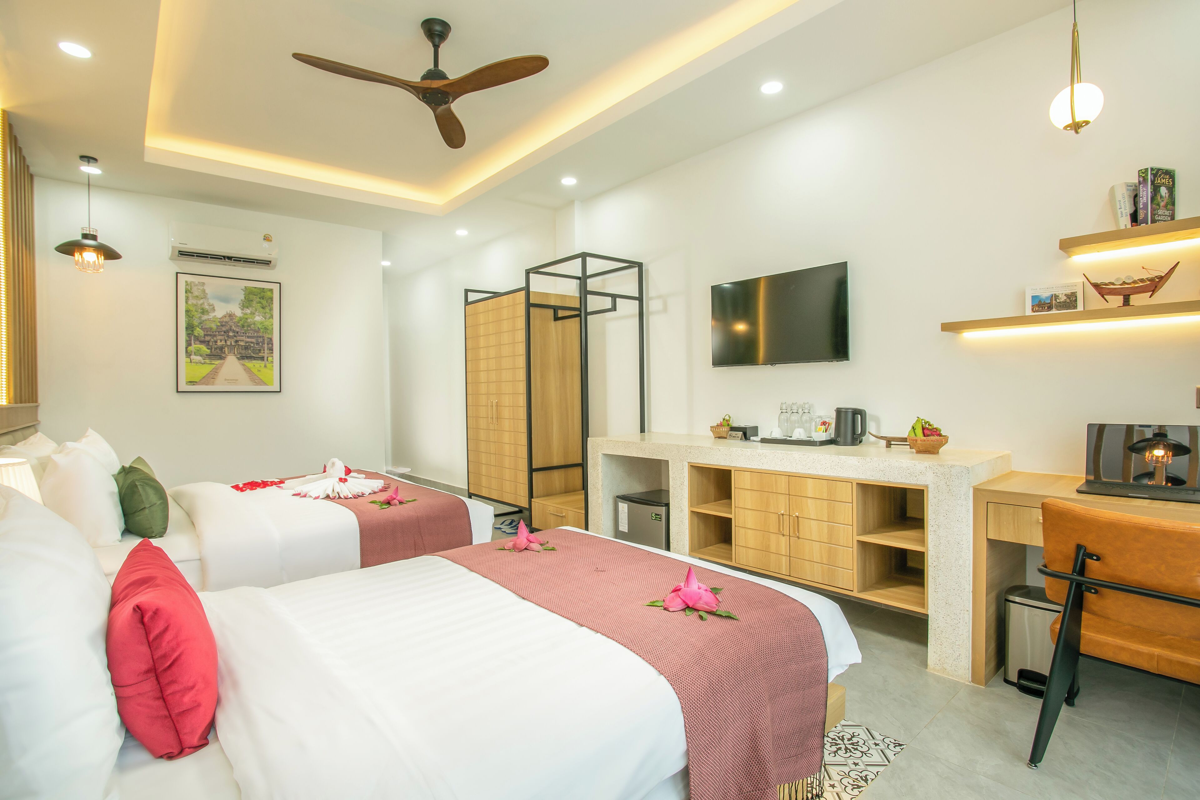 A hotel room with two beds, a desk, a TV, and a ceiling fan.