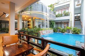 A hotel interior with a pool, indoor waterfall, and seating area.