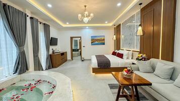Habitación de hotel con cama, sofá, una mesa de centro de madera, televisor y baño con bañera.