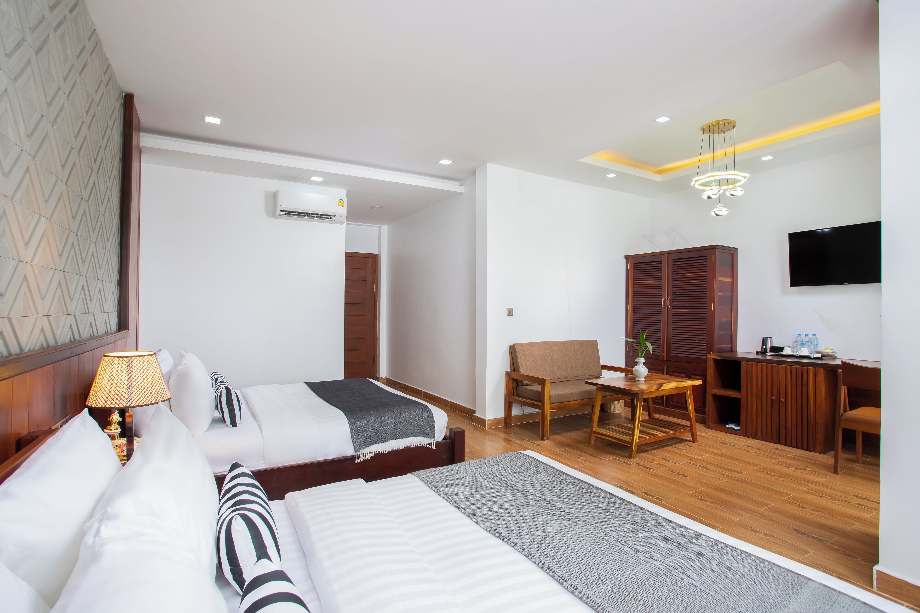 A hotel room with two beds, a desk, a chair, a TV, and an air conditioning unit.