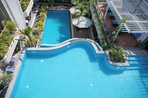 Une piscine sur le toit, dotée d’un bord incurvé, entourée de palmiers et agrémentée d’un espace salon extérieur.
