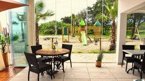 A patio area with a table and chairs, a view of a playground, and a beach in the background. - Bungalow on the sea - Moriani beach (Santa-Lucia-di-Moriani)