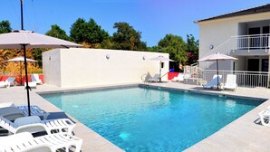 A swimming pool with lounge chairs and umbrellas, surrounded by a white fence and a building with a balcony. - Bungalow on the sea - Moriani beach (Santa-Lucia-di-Moriani)