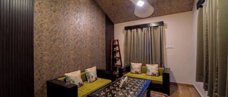 Uma sala de estar acolhedora com teto alto, ventilador de teto, parede estampada, conjunto de sofá, mesa de centro e tapete.