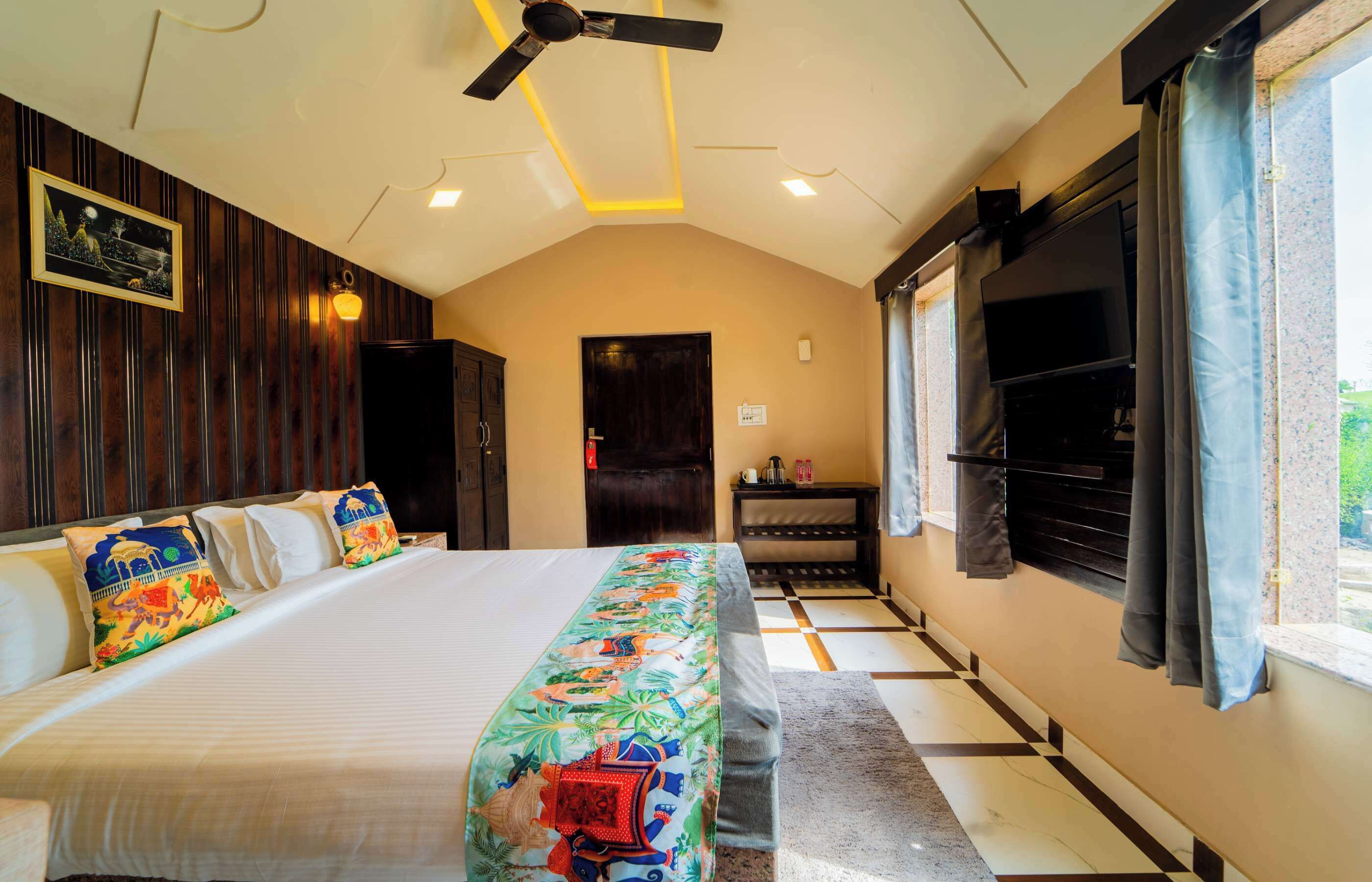 Habitación de hotel con cama, ventilador de techo, televisión y ventana con cortinas.
